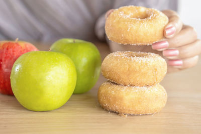 Woman hand holding donuts with sugar with apple in background