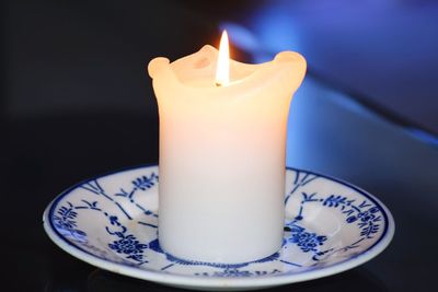 Close-up of lit candle in plate on table