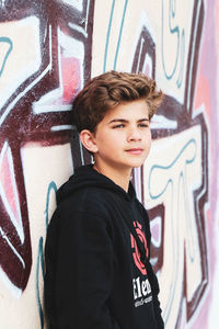 Portrait of young man standing against graffiti wall