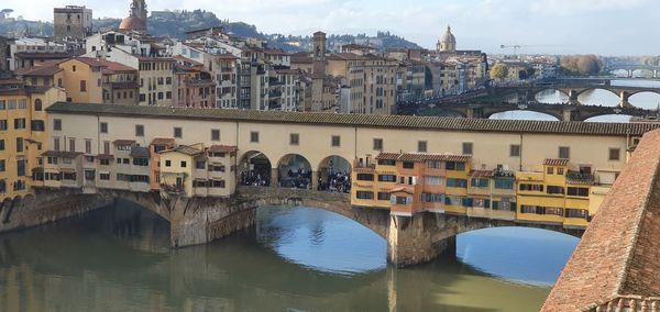 Arch bridge over river by buildings against sky