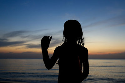 Silhouette girl with crab at beach against sky during sunset