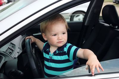 Baby boy looking away while sitting on drivers seat in car