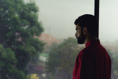 Portrait of man looking through glass window during rainy season