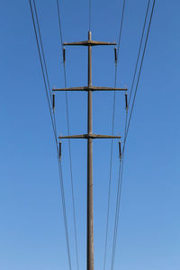 Low angle view of electricity pylon against clear blue sky