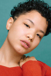 Portrait of young woman with her head bowed and hand on her shoulder, isolated vertical photo, tidewater green background