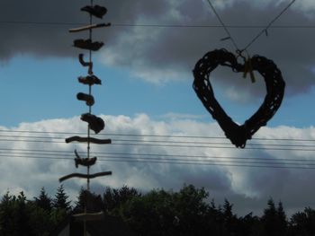 Low angle view of heart shape hanging on cable against sky