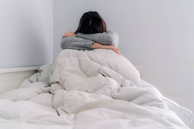 Rear view of woman sitting on bed at home