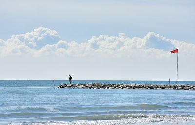 Man standing on groyne over sea against sky