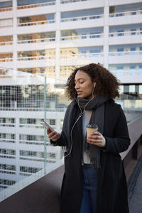 Beautiful woman with takeaway coffee and smartphone in city center