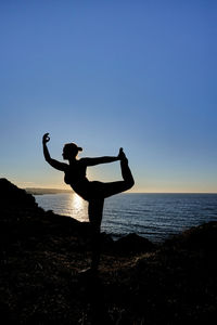 Rear view of man jumping on beach against clear sky