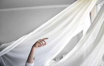 Cropped hand of woman against curtain at home