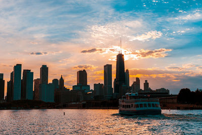 Modern buildings by sea against sky during sunset