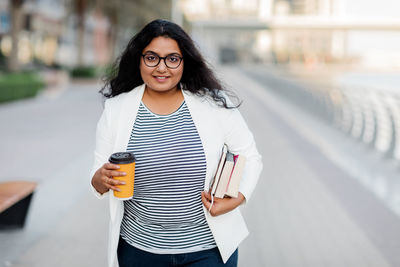 A beautiful young woman with a cup of coffee and books on the street.