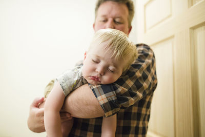 Low angle view of father carrying cute sleeping son while standing at doorway in house