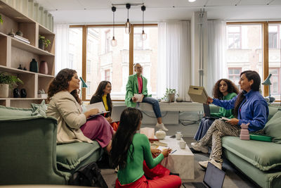 Female colleagues holding box while discussing with business coworkers during meeting at office