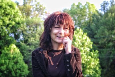 Portrait of smiling young woman standing against trees