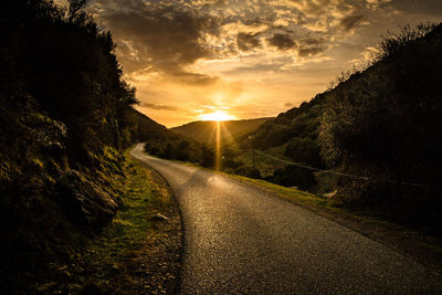 Road amidst trees against sky during sunset