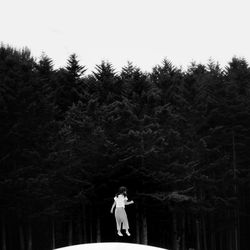 Woman standing by trees in forest against sky