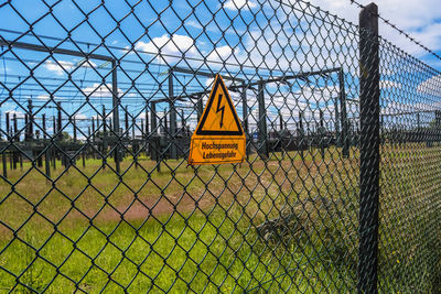 Information sign on chainlink fence against sky