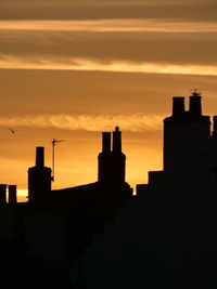 Silhouette of roof tops and chimney pots against orange sky