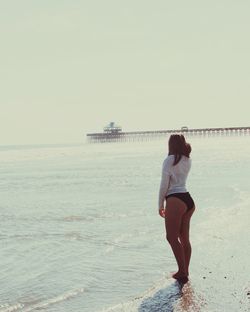 Full length rear view of woman standing on shore at beach against sky