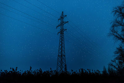 Silhouette of electric power lines tower, in the middle of a field against a night sky with stars