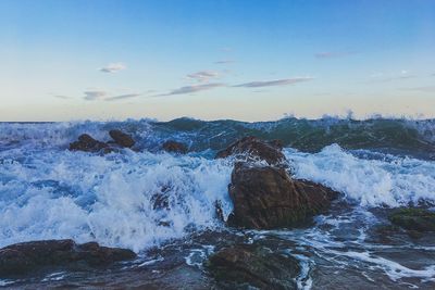 Waves splashing on rocks at shore against sky
