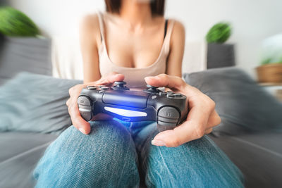 Midsection of woman playing video game while sitting on sofa at home