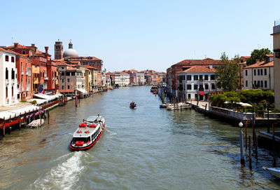 Boats moving on grand canal amidst buildings against clear blue sky