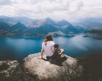 Rear view of man sitting on rock looking at mountains