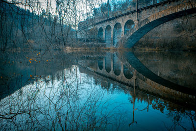 Arch bridge over river against bare trees