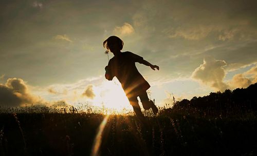 Silhouette boy on field against sky during sunset