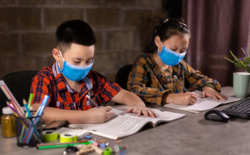 View of boy and girl wearing flu mask studying at home