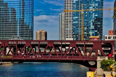 Bridge over river by buildings against sky in city