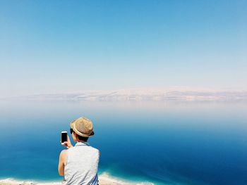 Rear view of woman photographing sea against clear sky