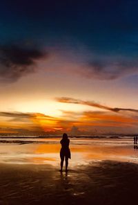 Silhouette woman walking at beach against sky during sunset