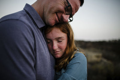 Daughter embracing father while standing on field during sunset