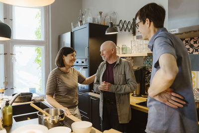 Smiling woman and man talking with senior father-in-law while standing in kitchen at home