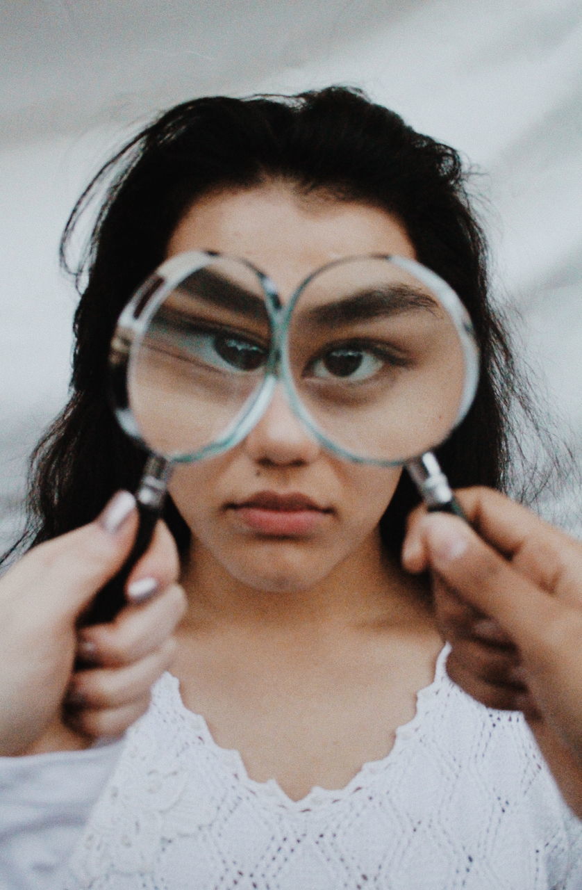 Portrait of young woman holding magnifying glass over eyes