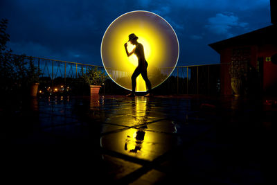 Side view of woman standing against circle shaped illuminated light at night