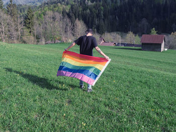 Rear view of man rainbow flag in field