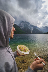 Man holding ice cream by lake against mountains