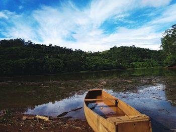 Boat moored on river by trees against sky