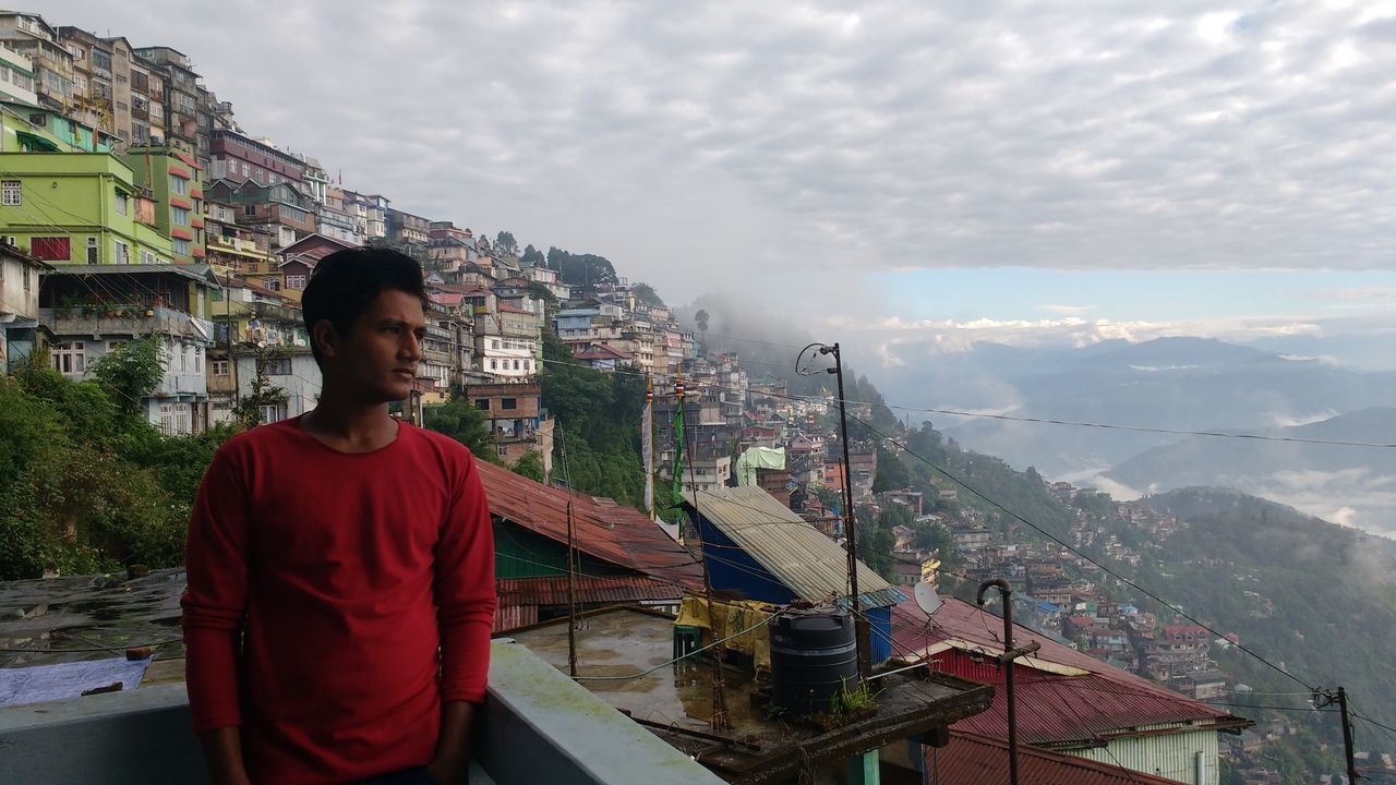 PORTRAIT OF MAN WITH CITYSCAPE IN BACKGROUND AGAINST SKY