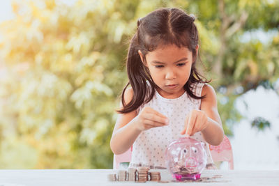 Girl putting coin in piggy bank at table