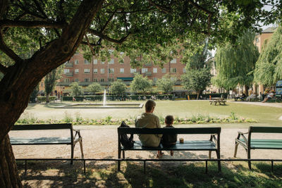 Rear view of man and grandson sitting on bench at park