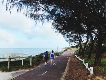 Rear view of people walking on road by sea