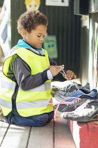 Boy in reflective jacket tying shoelace at porch