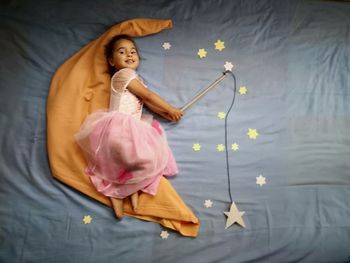 High angle view portrait of smiling girl with magic wand and stars on bed