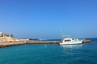 Boats in sea against clear blue sky